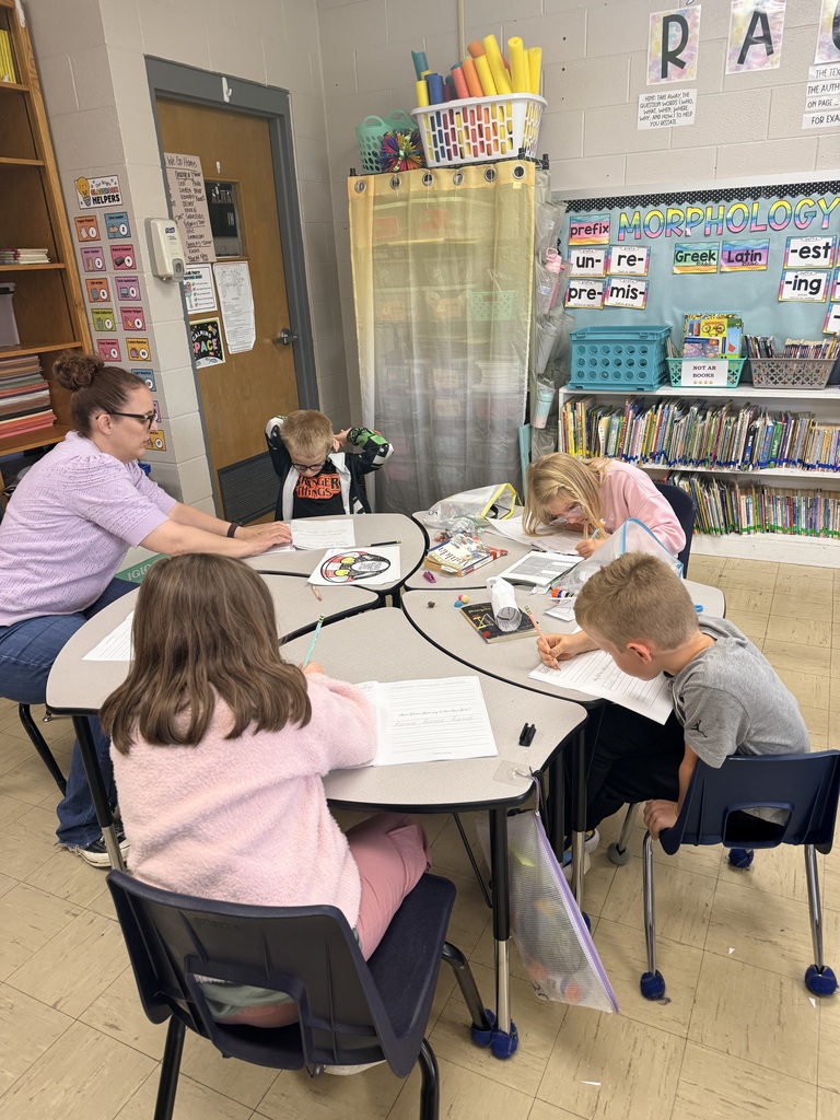 Photo showing an adult and  four third grade students and the worksheets they are practicing cursive on