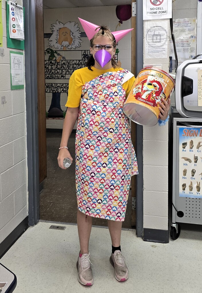 junior high student wrapped in heart wrapping paper and wearing 3 pointing birthday party hats--2 like they're ears, and one like a beak