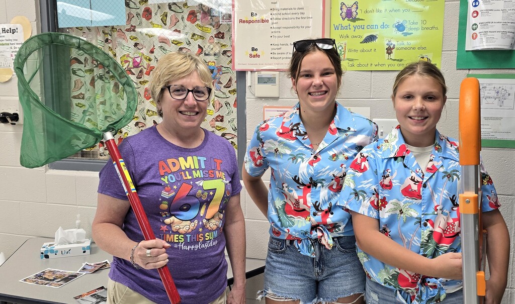 a science teacher with a net on a pole to catch a critter with 2 junior high students in matching Hawaiin shirts and one student is carrying a small ladder