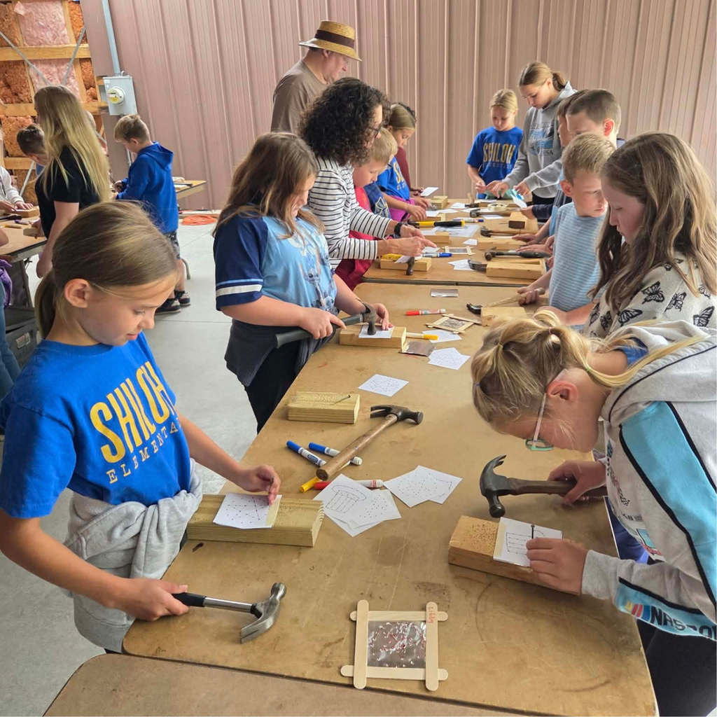3 tables of 4th grade students with hammers, nails, and blocks of wood creating a project
