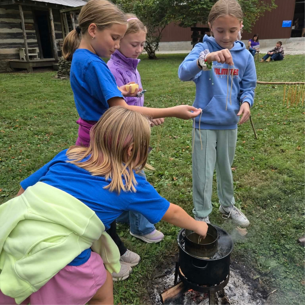 Four 4th grade students dip wicks in a can of melted wax to make candles