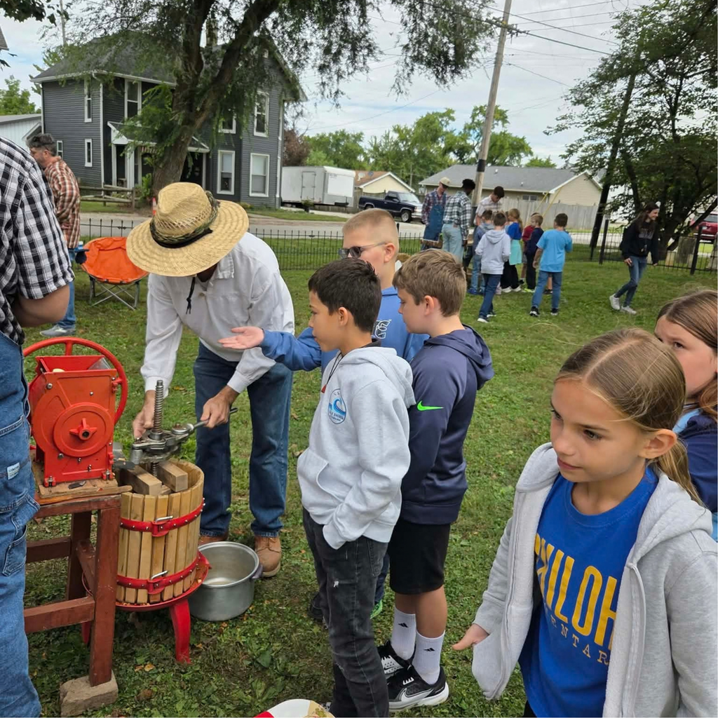 Photo of 4th graders in groups outside, including a group up front watching a gentlement press apples to make cider