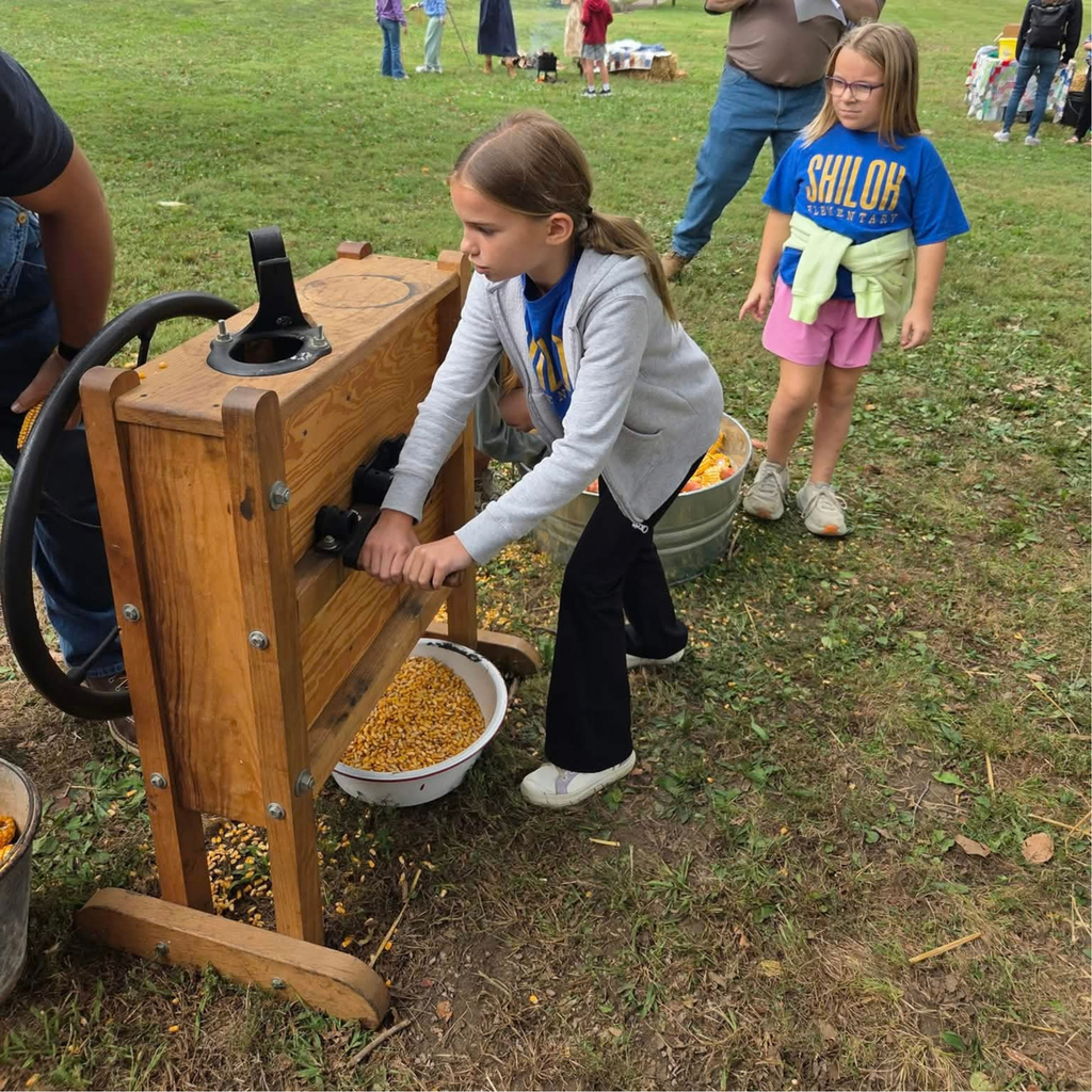 Two 4th grader girls take turns using an old hand-cranked machine to separate corn from the cob