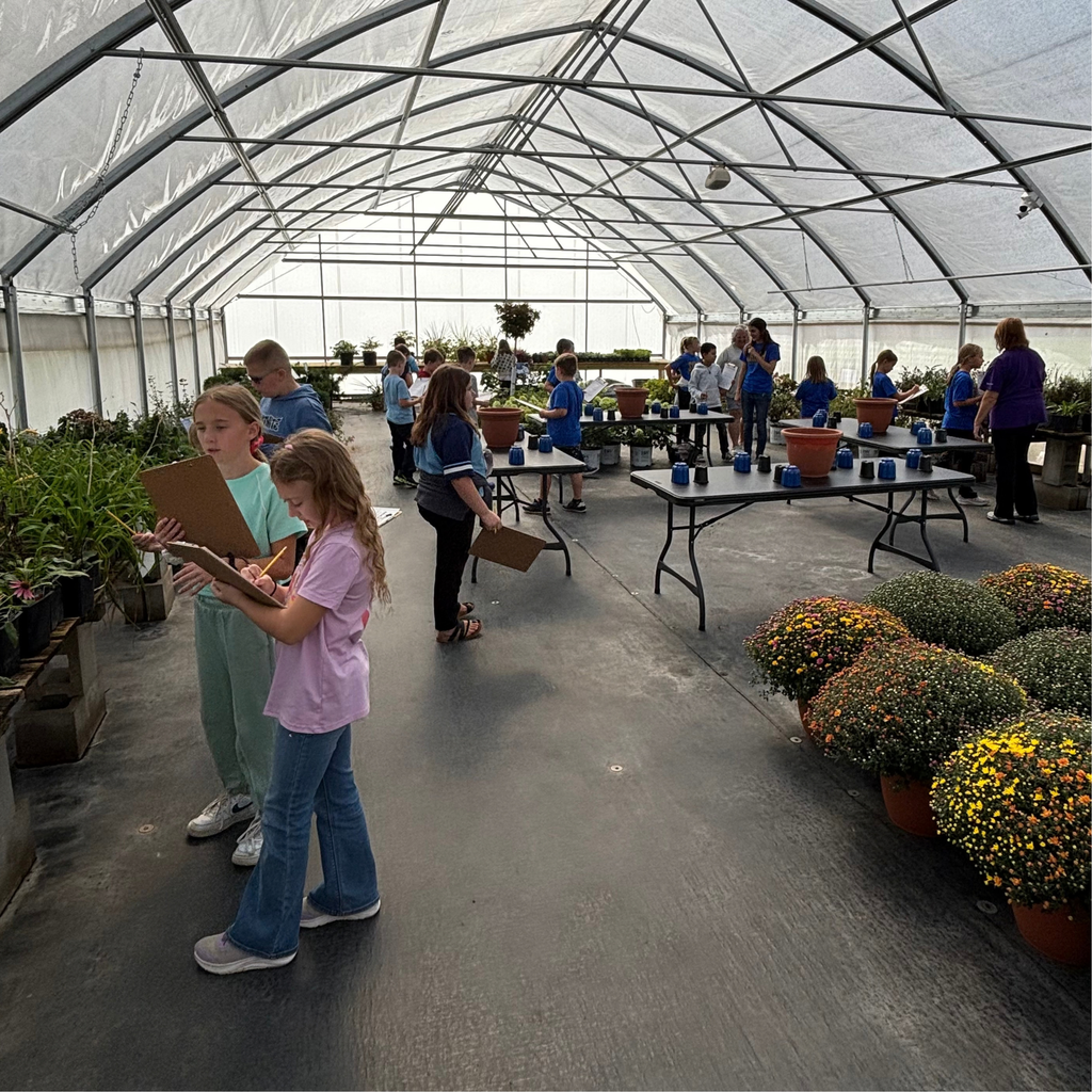 A greenhouse with tables throughout and mums in the front filled with 4th graders