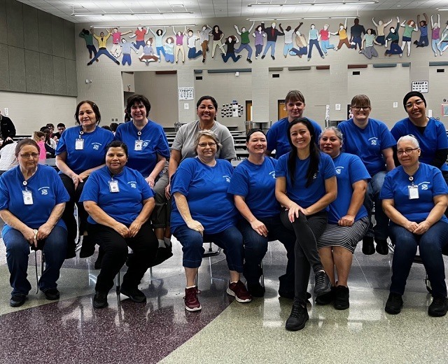 A group of people in blue shirts pose for a photo in a room with tiled flooring.