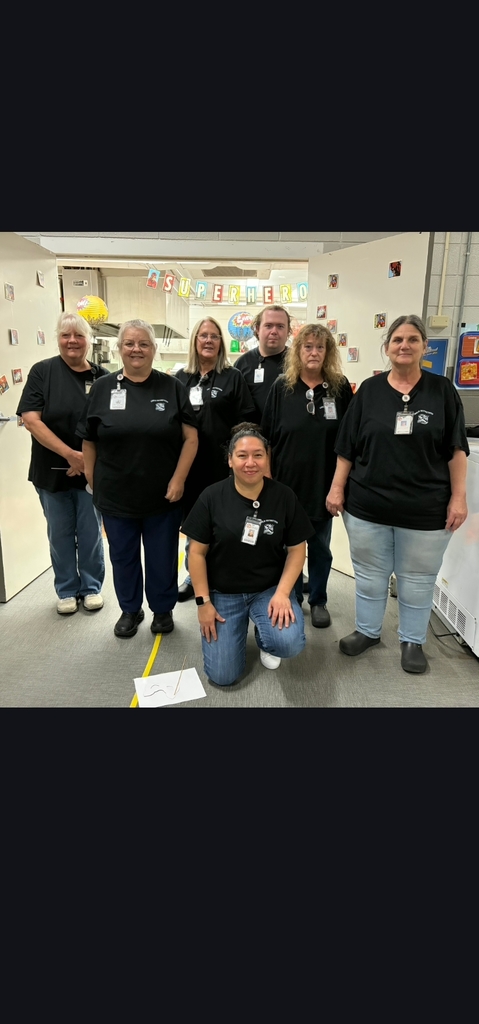 A group of seven people wearing black shirts and IDs pose for a photo in a room.