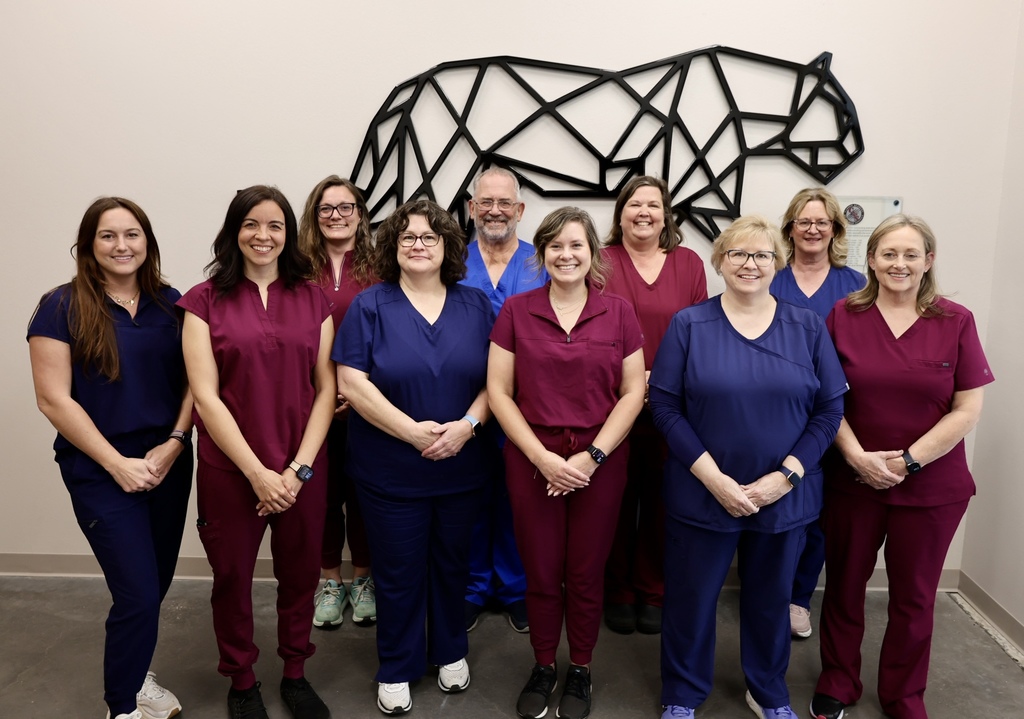 A group of 10 adults in matching uniforms pose in front of a wall with a black geometric bull sculpture.