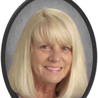 A woman with short blonde hair smiles at the camera. She has a light-colored top and is against a gray background.