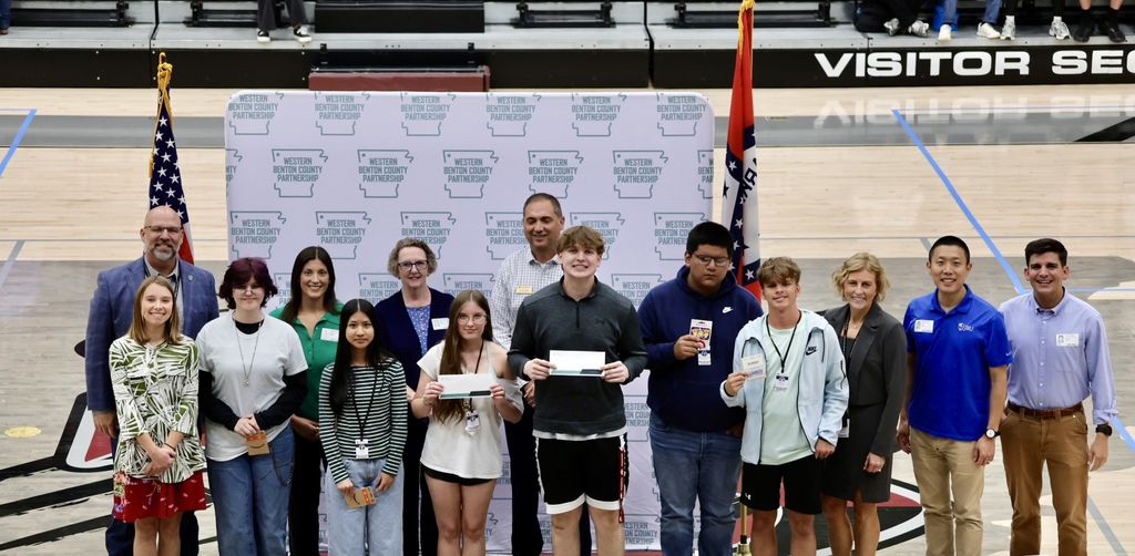 A group of people stand together, smiling, on a basketball court with an American flag in the background.