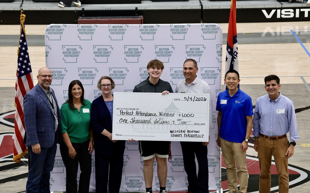 Group of people stand with a large check displayed. One person holds the check. They are in a sports venue.
