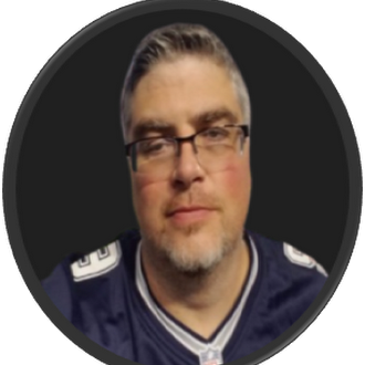 Man with a mustache and beard, wearing glasses, looking at the camera. He has on a blue football jersey.