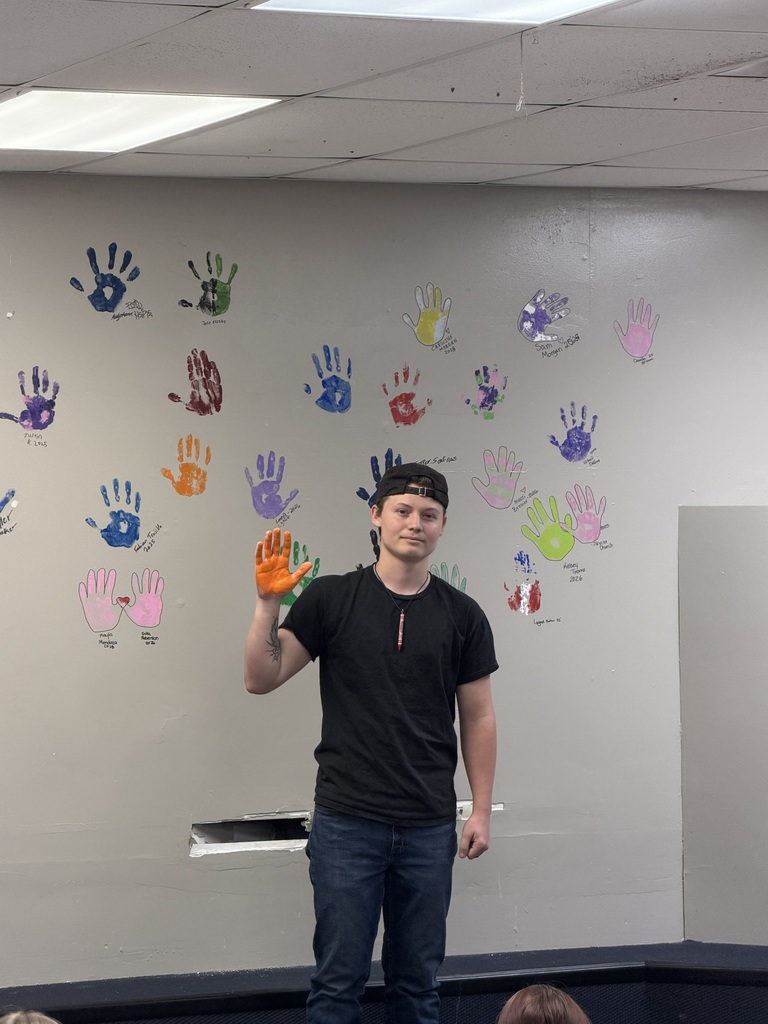 A person in a black t-shirt and jeans stands in front of a wall with multicolored handprints.