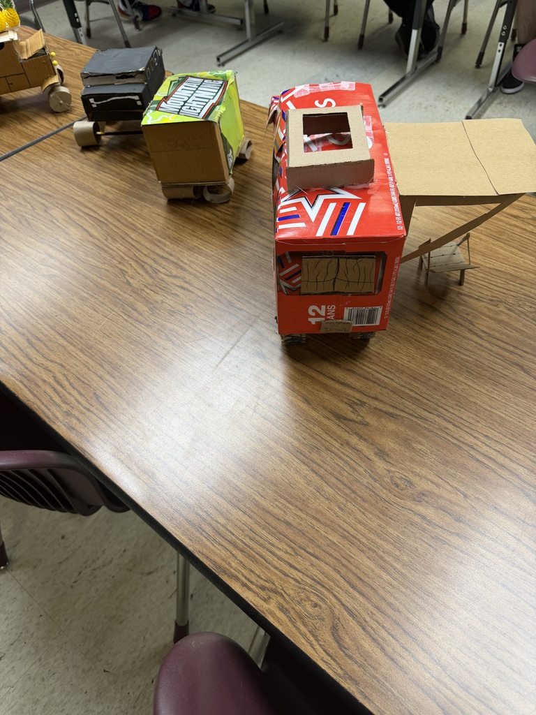 A wooden table has several cardboard boxes arranged on it. One is red with "SLE" written on it.