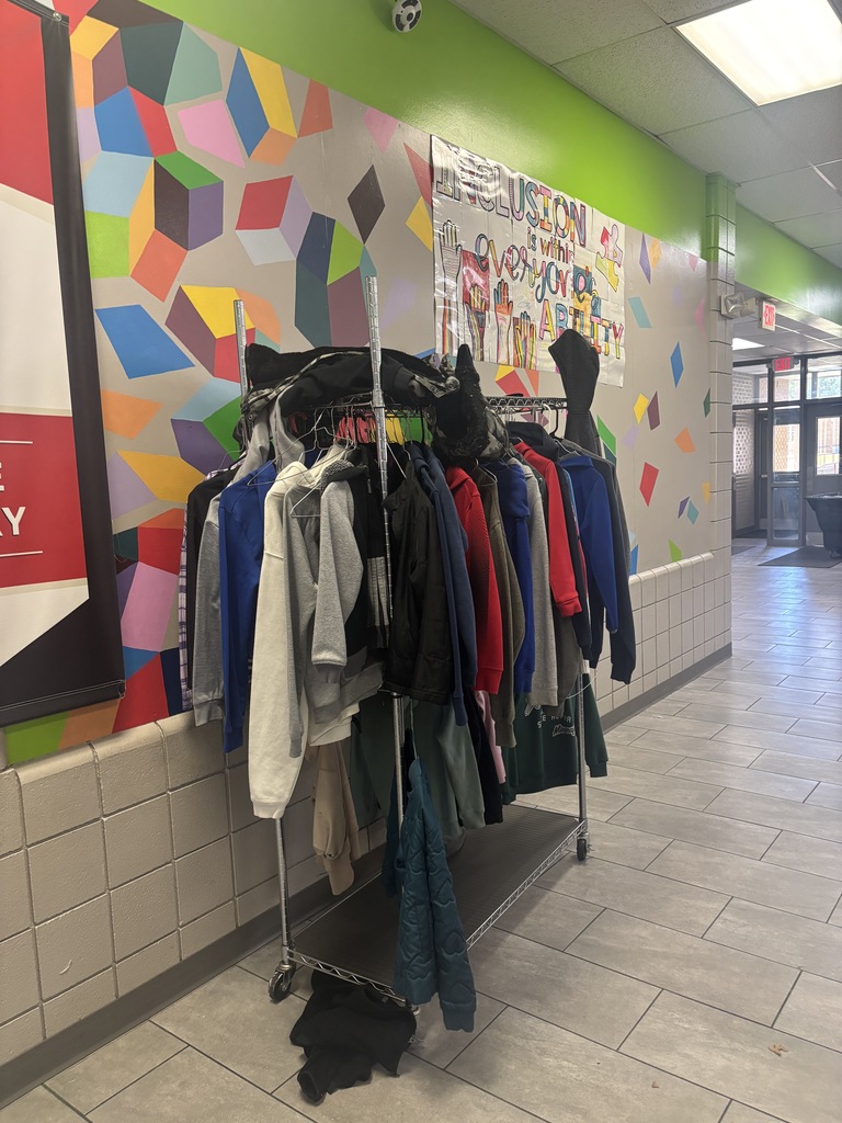 A hallway with a colorful geometric wall mural. A rack full of assorted clothing items is on the floor.