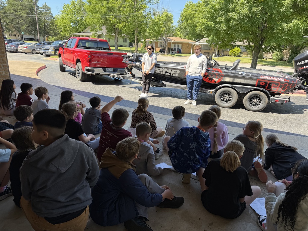 A group of people are sitting in a circle, with two individuals standing beside a red pickup truck.