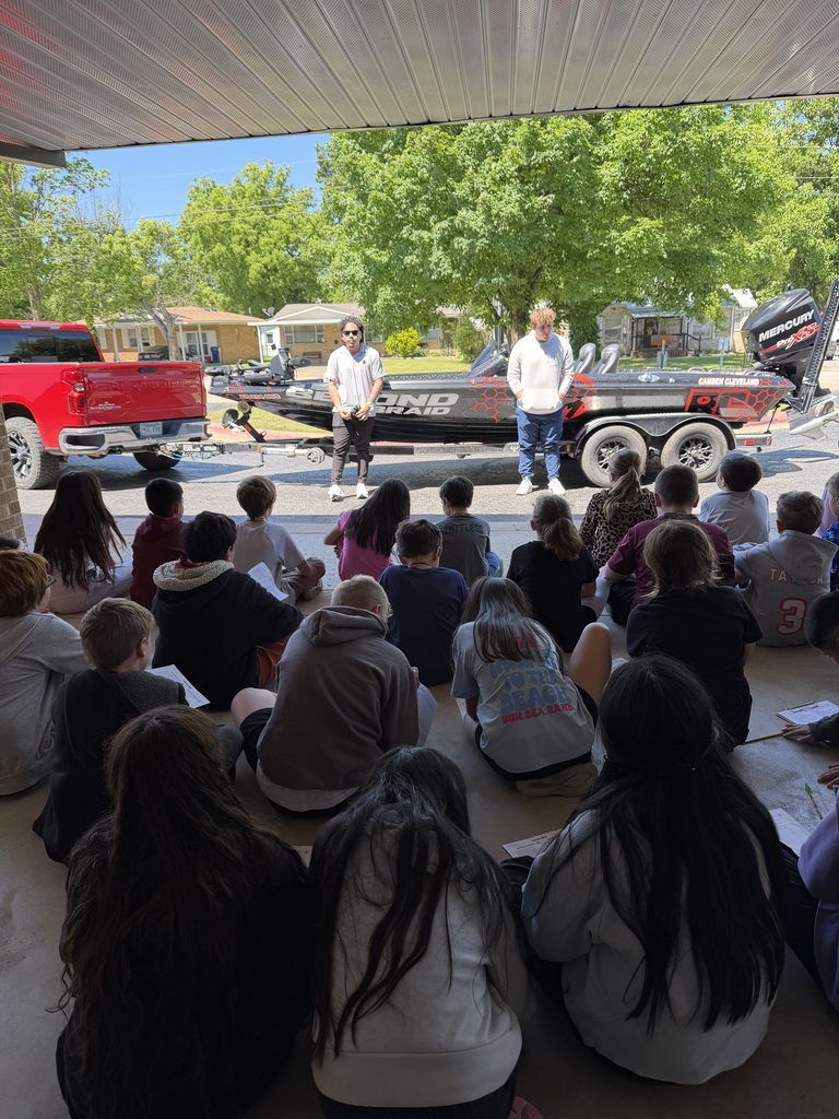 People gathered around a boat, listening to a presentation. One man stands in front of the boat.