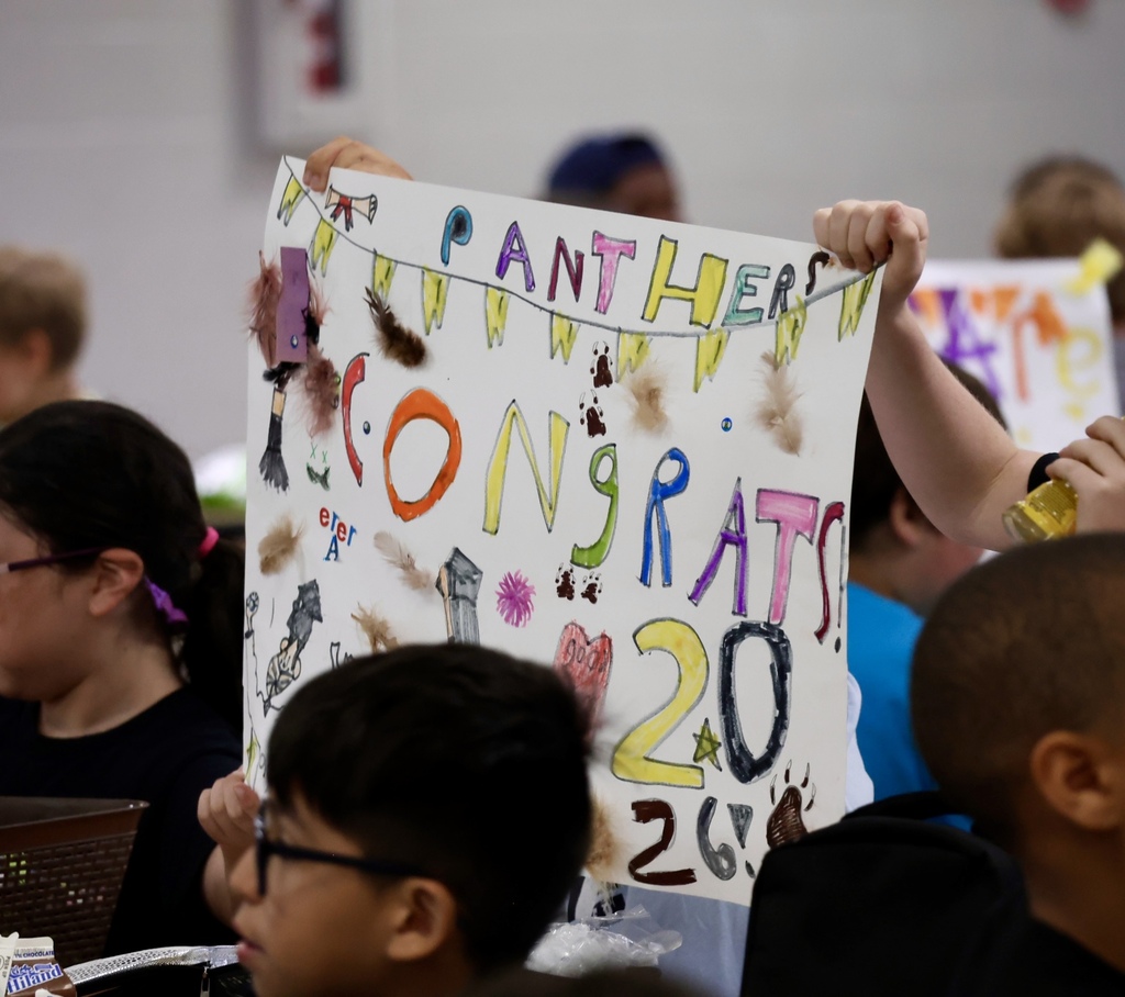 Students holding up a banner saying "Panthers CONGRATS 20 26". One student wearing glasses.
