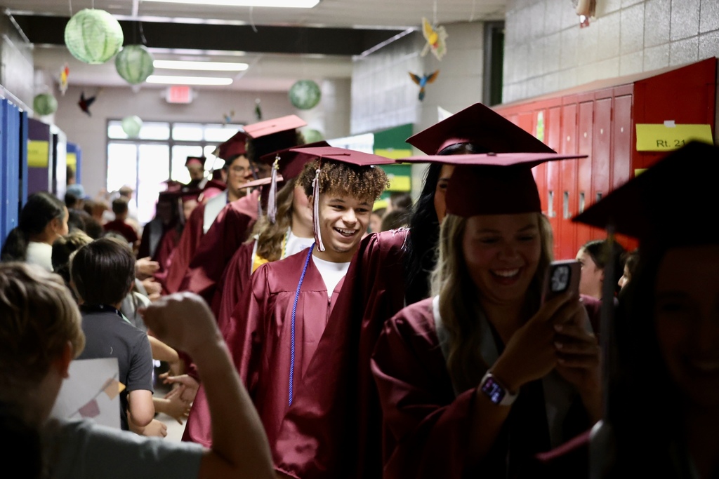 A hallway filled with students wearing caps and gowns, smiling and posing for photos.