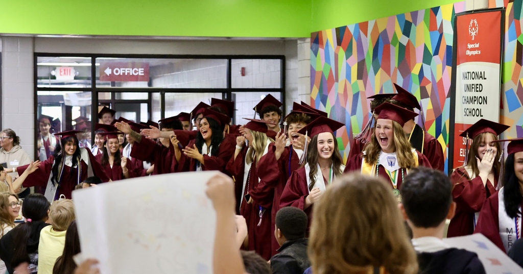 A group of people in graduation gowns and caps are celebrating together. Some are cheering.
