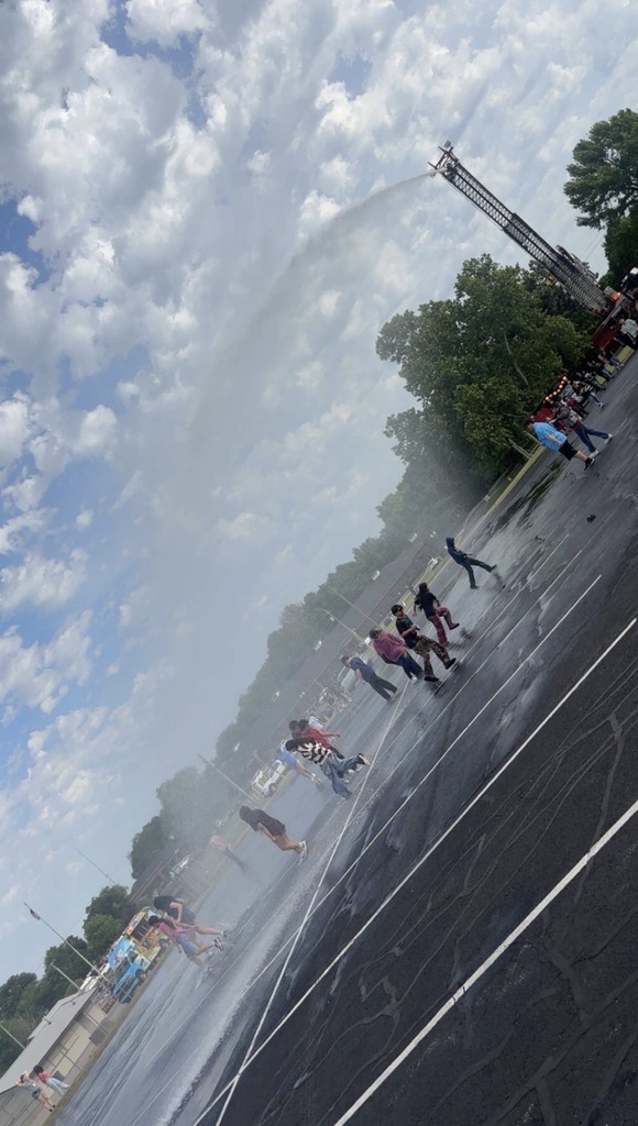 A group of students running through the spray from the hose of the fire truck.