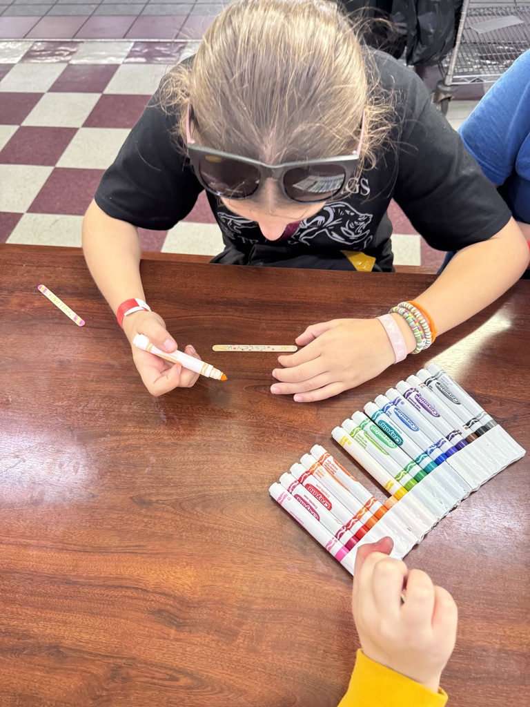 A student drawing on their popsicle stick for the mural that is being created.