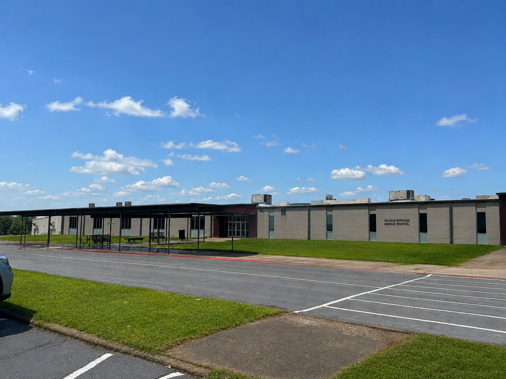 A school building with a large carport and a grassy lawn in front. Blue sky with clouds.
