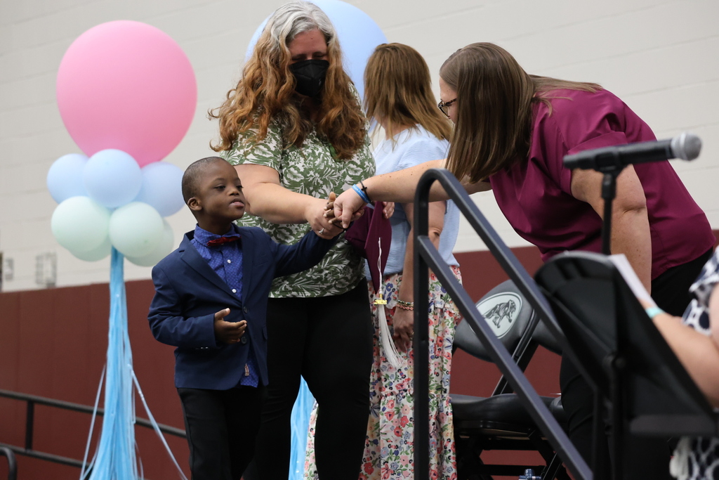 A young boy in a suit is shaking hands with adults. One is wearing a face mask.