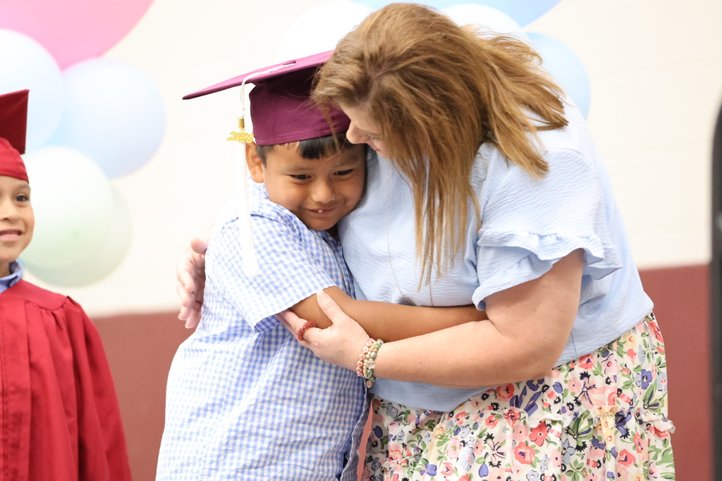 A young boy in a cap hugs an adult woman who has her hands around him. A child stands in the background.