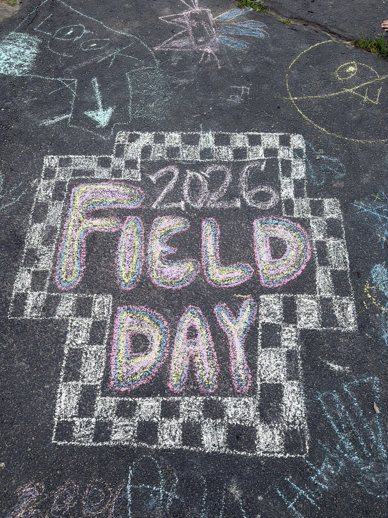 A sidewalk with chalk artwork. A large checkered square with "2026 FIELD DAY" written in vibrant colors.