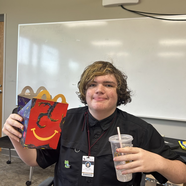 A student holding up the happy meal that he won.