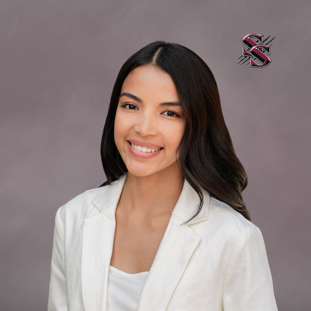 A woman with long black hair and a white blazer smiles at the camera. Background is gray, with a red logo.