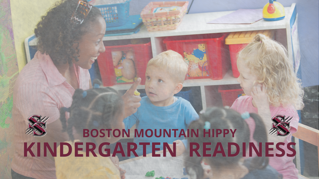 Woman with dark hair talks to children in a classroom. Four kids sit around a table, listening.