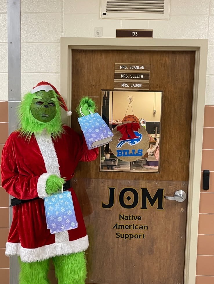 Student in Grinch costume holding holiday gift bags