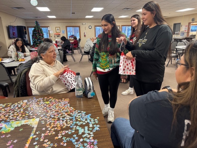 Three students give a gift bag to an elder. 