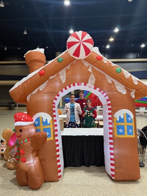 Three students pose in an inflatable gingerbread house. 