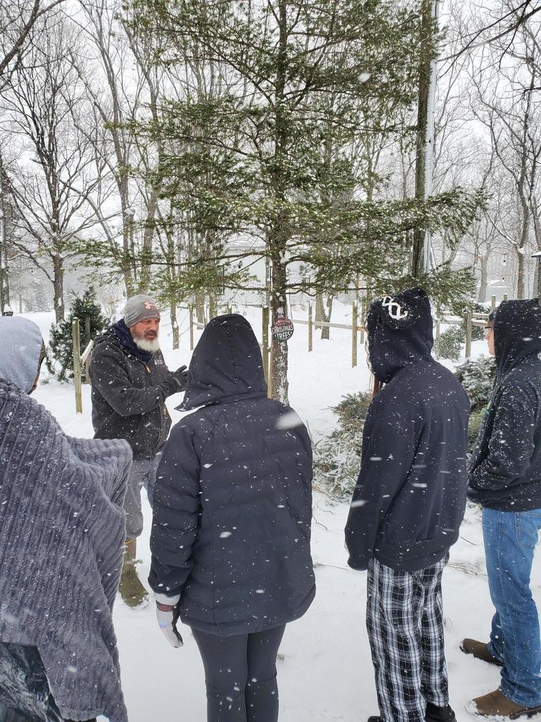 Students learn about a Christmas tree farm while outside in the snow. 