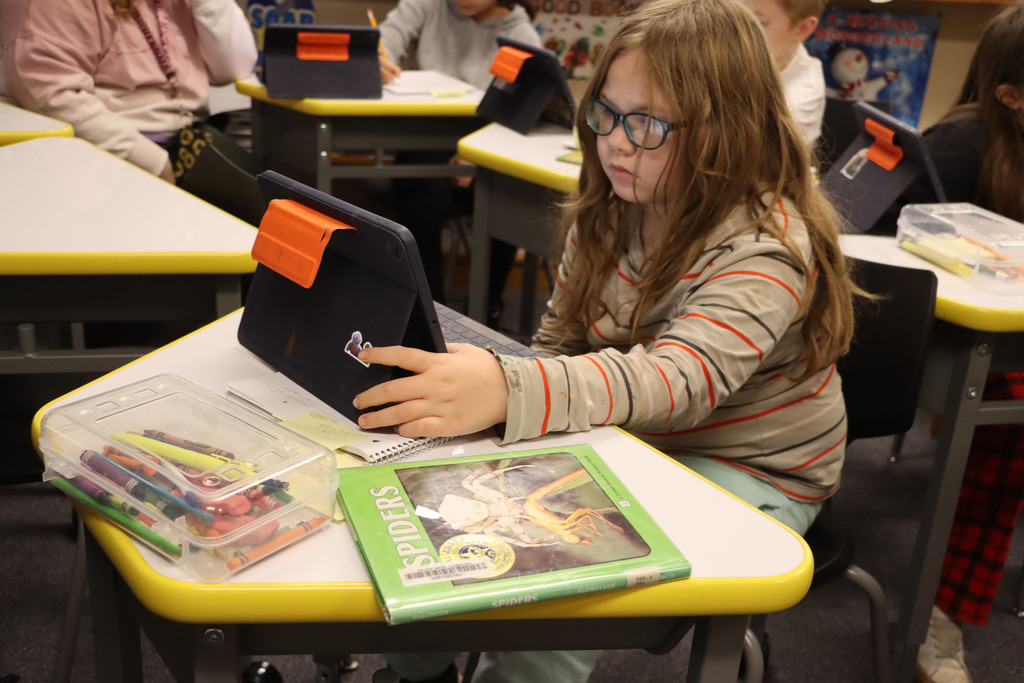 A student uses a spider book and her iPad to do a research project, 