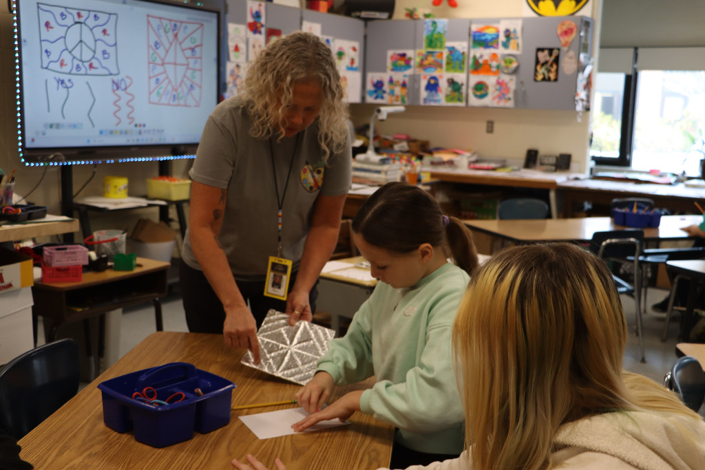 teacher shows a foil example of the project to two students.