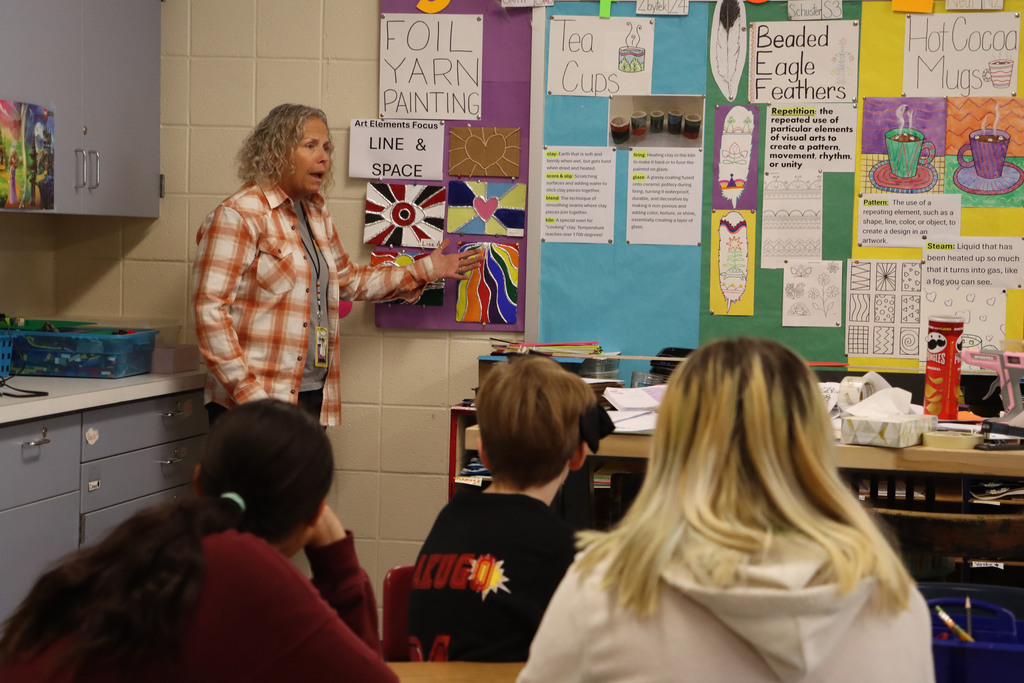 teacher shows examples of the project on the bulletin board, including hearts, an eye and a landscape. 
