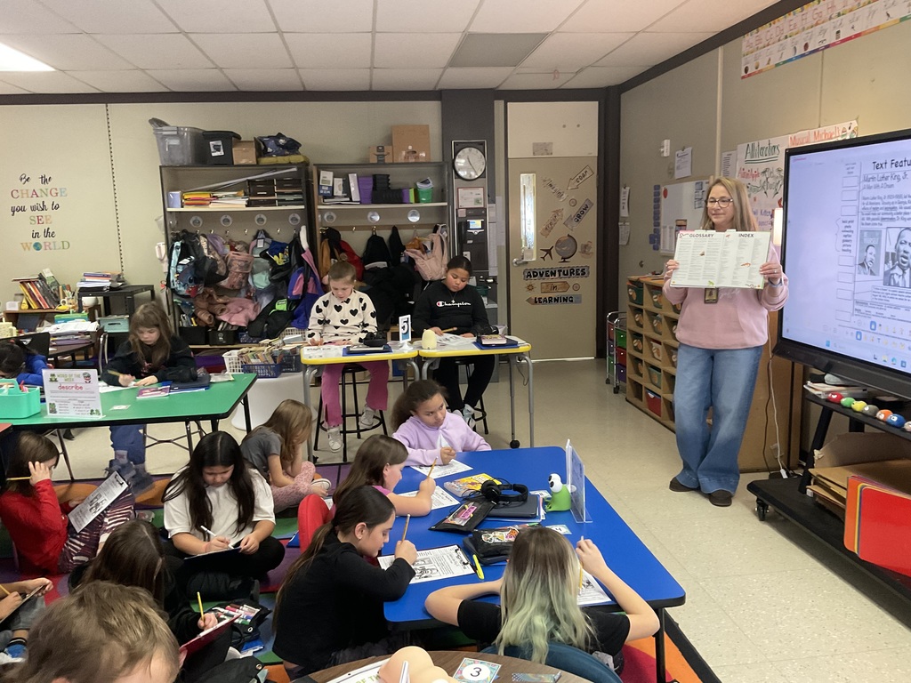A teacher holds up a paper as students work. 