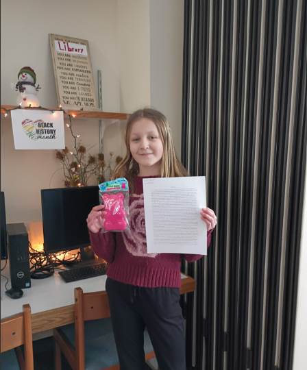 Ava in the library holding her short story and a gummy bear toy prize