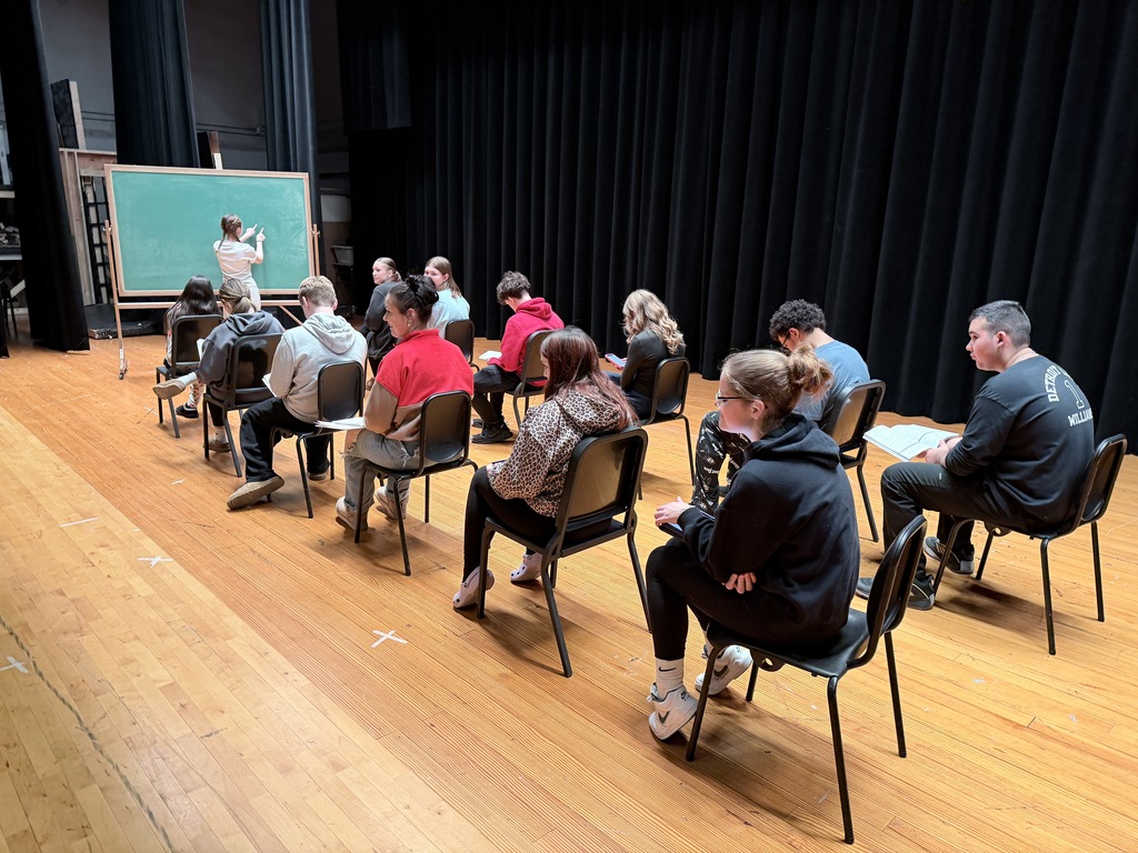 students act as if they are in a classroom on stage.