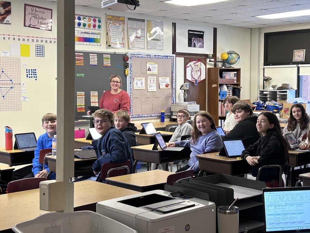 Mrs. Cave in the front of her classroon with students smiling at desks