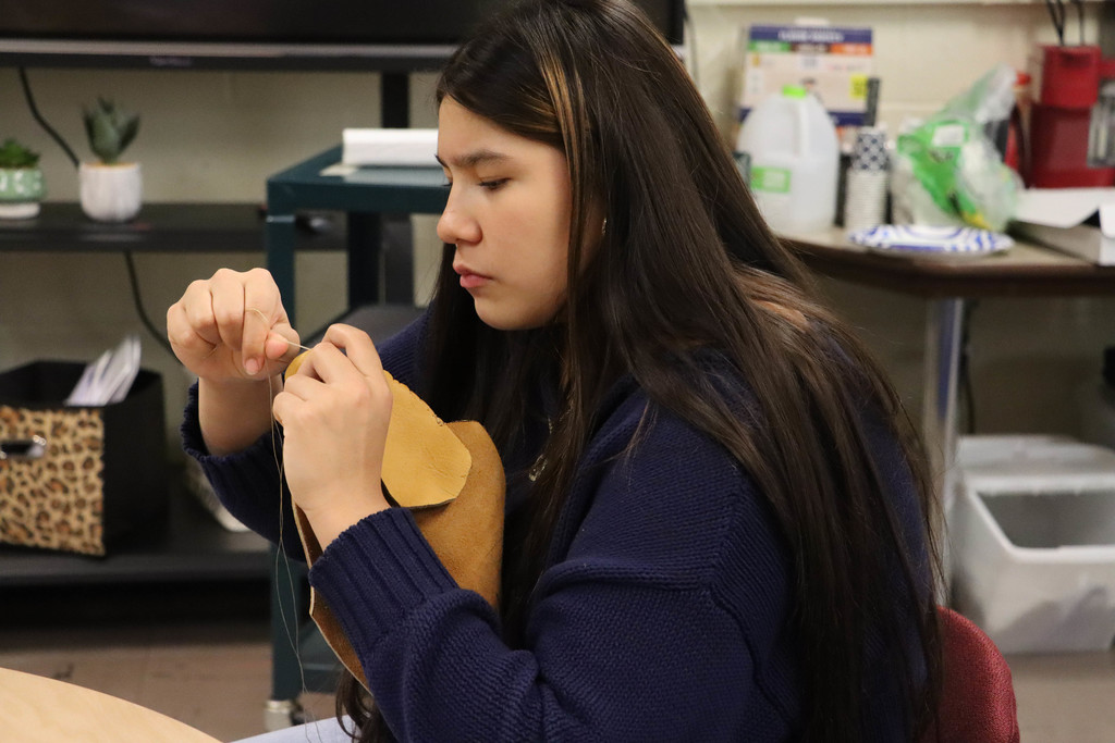 a student sews her moccasin