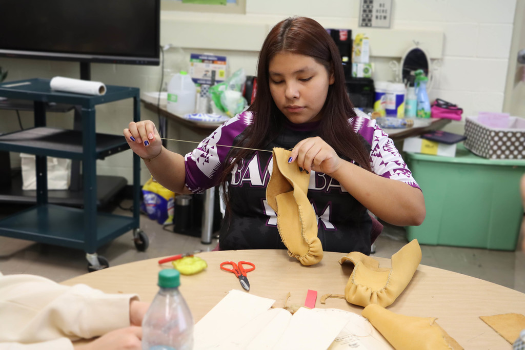 a student sews her moccasin