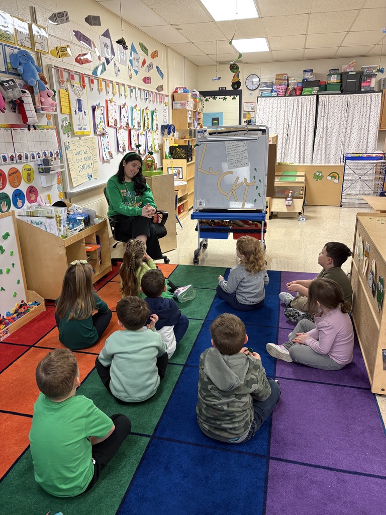 Miss Lattanzio speaks to her students seated on a carpet