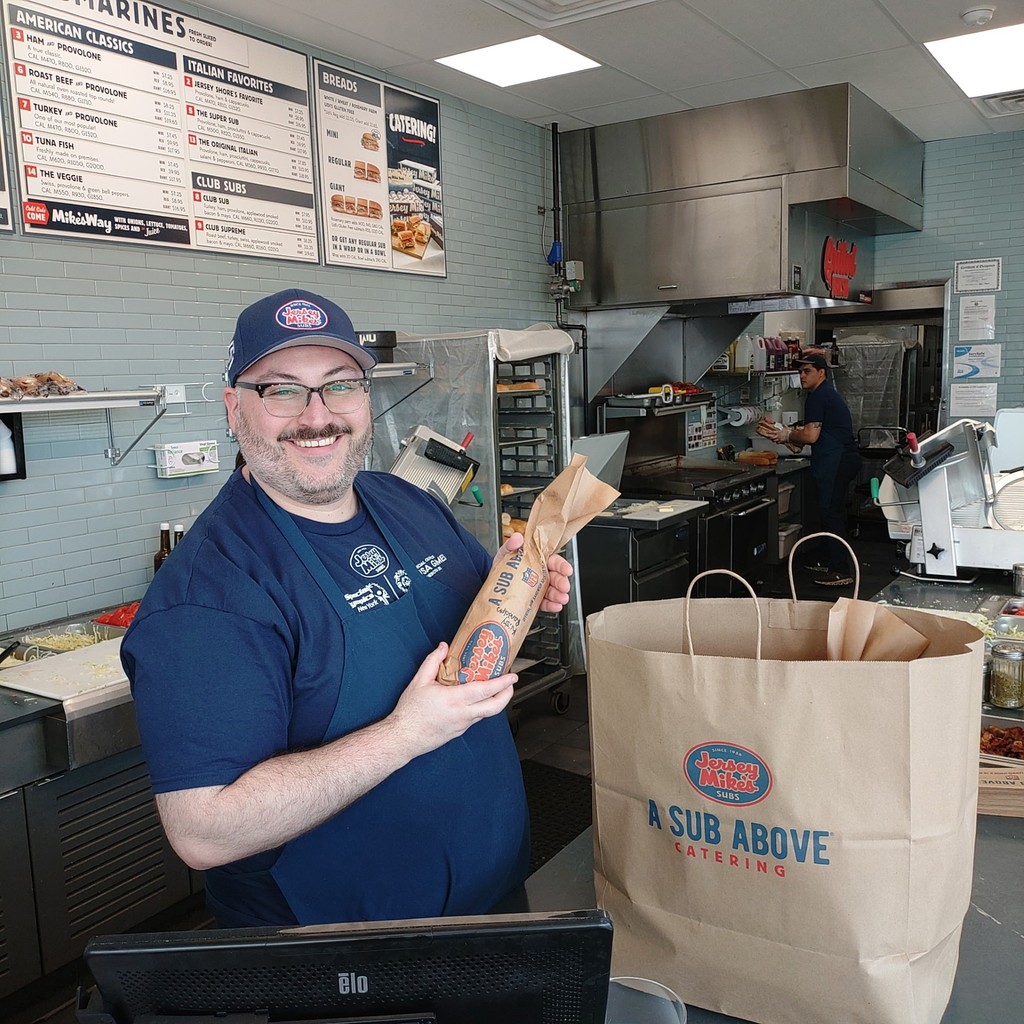 Man smiling adding wrapped sub to a paper bag