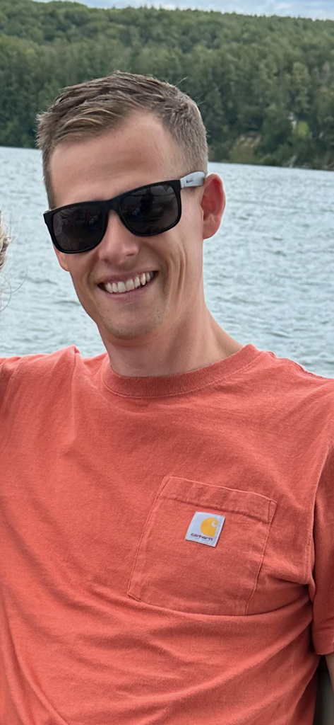 Mr. Bratcher smiling with water and landscapre in the background