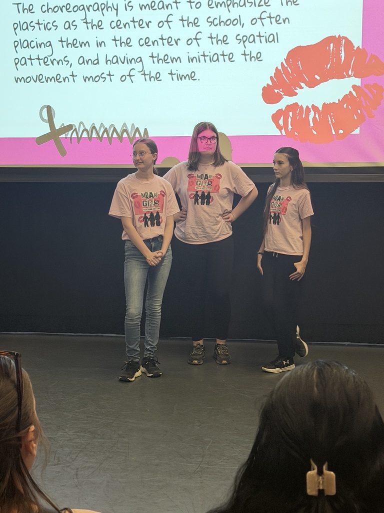 three female students ons tage in front of projection screen