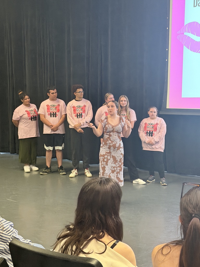 Ms. Jasinski on stage with student cast, speaking to audience